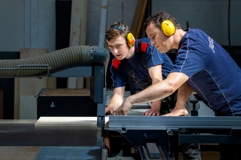 Twee medewerkers in de productiehal aan het werk met hout snijden.