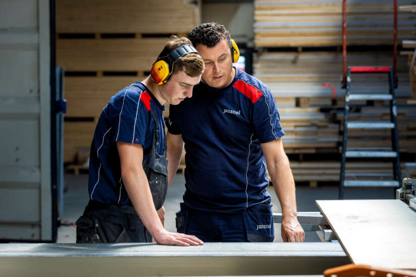 Twee medewerkers met oorbeschermers kijken naar een plank in de houtzagerij.
