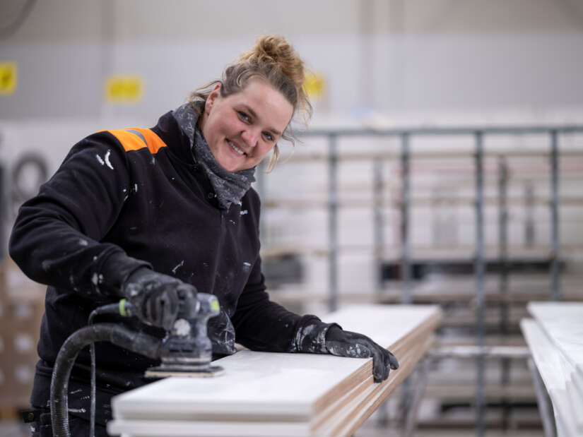 Medewerker vrouw in werkkleding hout aan het schuren