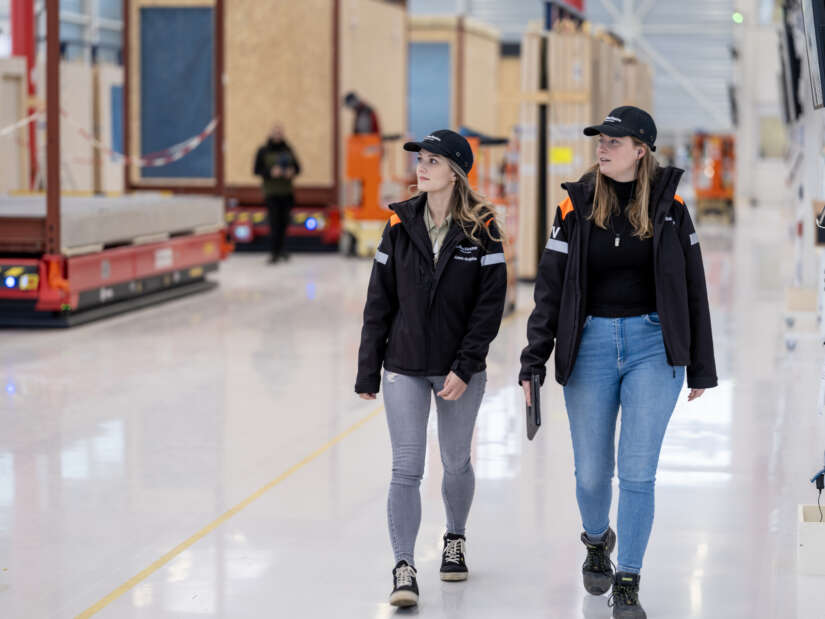Vrouwen in werkkleding lopen door de productiehal.