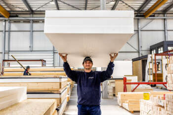 Medewerker in de fabriek draagt een pak materiaal boven zijn hoofd.