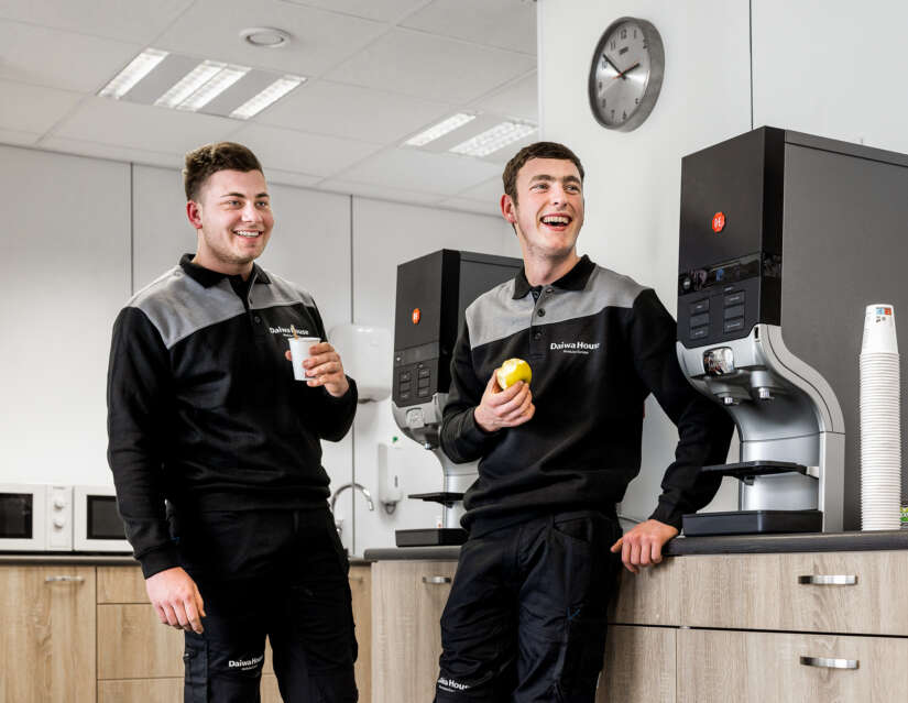 Twee lachende medewerkers bij het koffiezetapparaat in de kantine van Daiwa House Modular Europe.